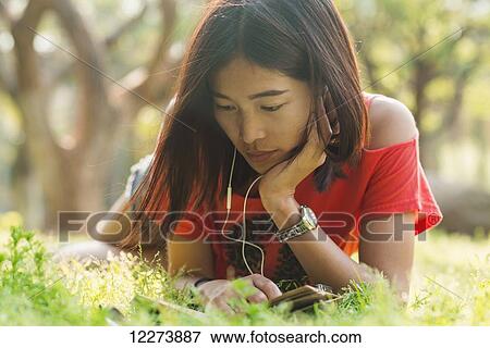 Stock Photo - Chinese girl reading a book and listening to music; Xiamen, Fujian Province, China. Fotosearch