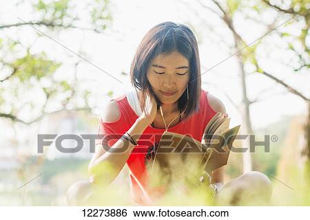 Stock Photograph - Chinese girl reading a book and listening to music; Xiamen, Fujian Province, China. Fotosearch