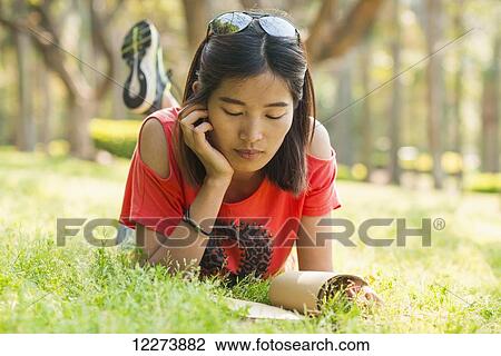 Stock Image - Chinese girl reading a book on the grass; Xiamen, Fujian Province, China. Fotosearch