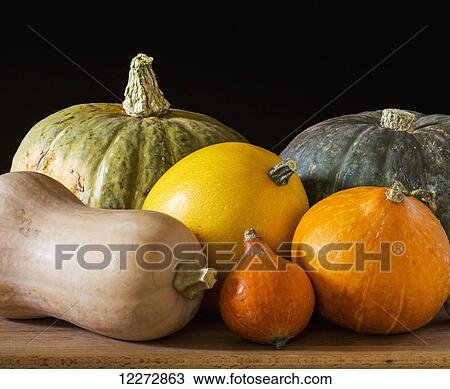 Stock Image - Close up of assorted colours and shapes of squash on a wooden board and black background; Calgary, Alberta, Canada. Fotosearch