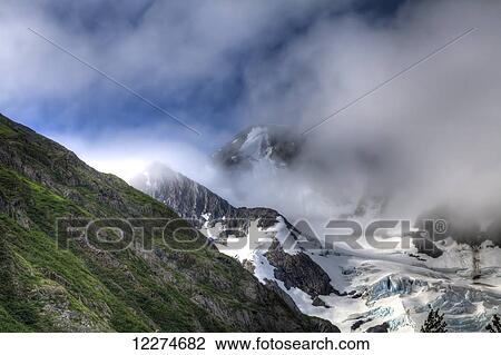Stock Image - Clouds breaking around Byron Glacier in Portage Valley, Chugach National Forest; Alaska, United States of America. Fotosearch