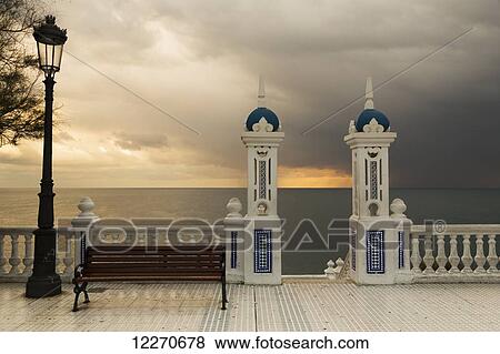 Stock Photo - Decorative railing and pillars on the promenade with a bench and lamppost at sunset; Benidorm, Spain. Fotosearch