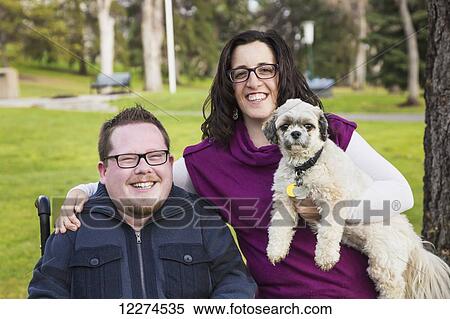 Stock Photography - Disabled husband and his wife and their pet dog posing for a family portrait in a park in autumn; Edmonton, Alberta, Canada. Fotosearch