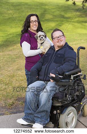 Stock Image - Disabled husband with his wife and their pet dog posing for a family portrait in a park in autumn; Edmonton, Alberta, Canada. Fotosearch