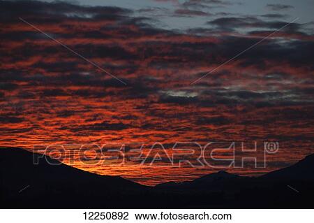 Stock Image - Dramatic red sunset over silhouetted landscape; New Zealand. Fotosearch