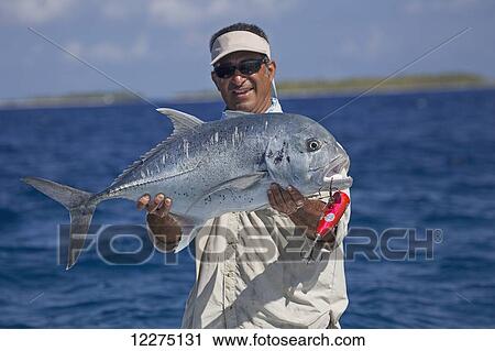 Stock Image - Fisherman holding a giant trevally fish (Caranx ignobilis); Tahiti. Fotosearch