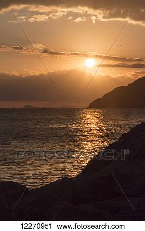 Stock Image - Golden sun setting with silhouette of hills along the mediterranean coastline; Benidorm, Spain. Fotosearch