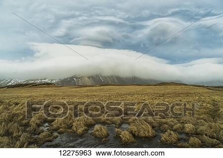 Stock Image - High winds create lenticular clouds in the upper atmosphere over the Eastern Fjords in Southeastern Iceland; Iceland. Fotosearch