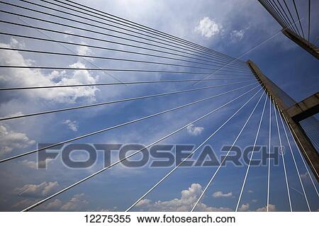 Stock Photography - Looking up through the suspension cables of a large modern bridge to the concrete tower structure of the bridge and a blue sky with clouds; United States of America. Fotosearch