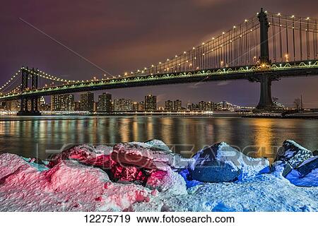 Stock Photo - Manhattan Bridge by snow-covered rocks at sunset, Brooklyn Bridge Park; Brooklyn, New York, United States of America. Fotosearch