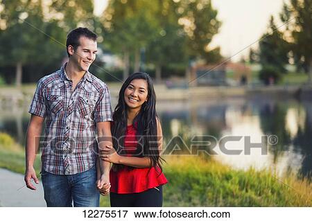 Stock Photo - Mixed race couple spending quality time together walking around a lake in a park in autumn; St. Albert, Alberta, Canada. Fotosearch