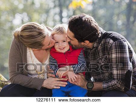 Stock Image - Mother and father kissing their son in a park in autumn; Langley, British Columbia, Canada. Fotosearch