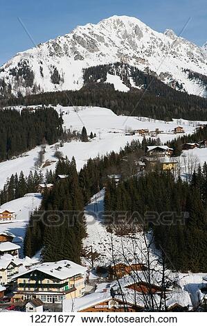 Stock Photo - Mountains, ski slopes, snow-covered wooden houses and fir trees in the Alpine ski resort; Filzmoos, Austria. Fotosearch