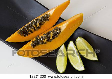 Stock Image - Papaya and lime slices on a black platter; Chilliwack, British Columbia, Canada. Fotosearch