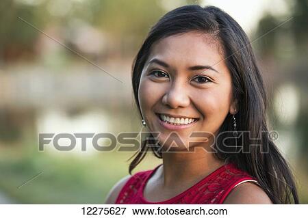 Stock Photo - Portrait of a beautiful young Filipino woman smiling in a city park in autumn; St. Albert, Alberta, Canada. Fotosearch