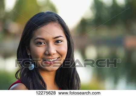 Stock Photo - Portrait of a beautiful young Filipino woman smiling in a city park in autumn; St. Albert, Alberta, Canada. Fotosearch