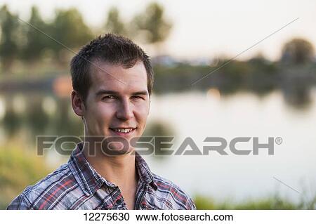 Stock Image - Portrait of a young man beside a lake in autumn; St. Albert, Alberta, Canada. Fotosearch