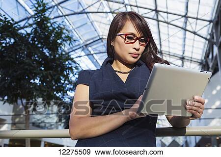 Professional businesswoman using her tablet to conduct business in a shopping mall; St. Albert, Alberta, Canada View Large Photo Image Stock Photo - Professional businesswoman using her tablet to conduct business in a shopping mall; St. Albert, Alberta, Canada. Fotosearch