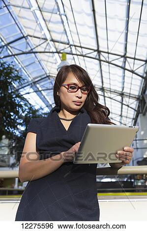 Stock Photograph - Professional businesswoman using her tablet to conduct business in a shopping centre; St. Albert, Alberta, Canada. Fotosearch