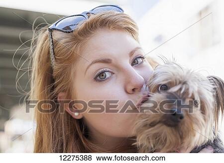 Stock Photo - Red haired young woman holding and kissing her small dog; United States of America. Fotosearch