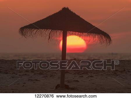 Silhouette of a beach umbrella on the beach with a colourful sun sinking into the horizon over the ocean; Tarifa, Cadiz, Andalusia, Spain View Large Photo Image Stock Photograph - Silhouette of a beach umbrella on the beach with a colourful sun sinking into the horizon over the ocean; Tarifa, Cadiz, Andalusia, Spain. Fotosearch