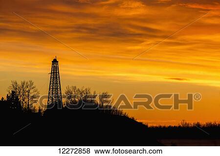 Silhouette of an old wooden drilling rig on tree covered hillside with dramatically colourful clouds at sunrise; Calgary, Alberta, Canada View Large Photo Image Stock Photo - Silhouette of an old wooden drilling rig on tree covered hillside with dramatically colourful clouds at sunrise; Calgary, Alberta, Canada. Fotosearch