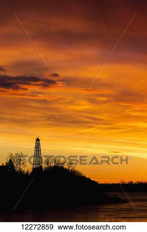 Silhouette of an old wooden drilling rig on tree covered hillside with dramatically colourful clouds at sunrise; Calgary, Alberta, Canada View Large Photo Image Stock Photo - Silhouette of an old wooden drilling rig on tree covered hillside with dramatically colourful clouds at sunrise; Calgary, Alberta, Canada. Fotosearch