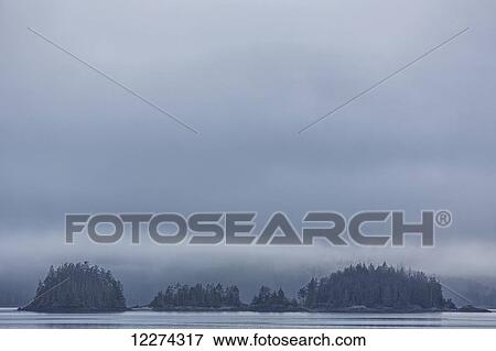 Stock Photo - Small islands covered with trees in the fog; British Columbia, Canada. Fotosearch