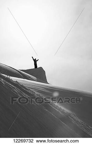 Stock Image - Snowboarder standing on a snow covered mountain ridge with arms raised; Haines, Alaska, United States of America. Fotosearch