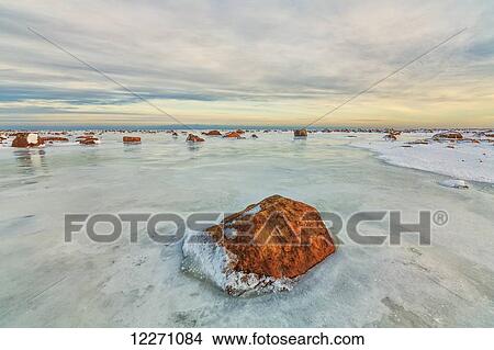 Picture - Sunset lights up the rocks and ice covered Hudson Bay; Manitoba, Canada. Fotosearch