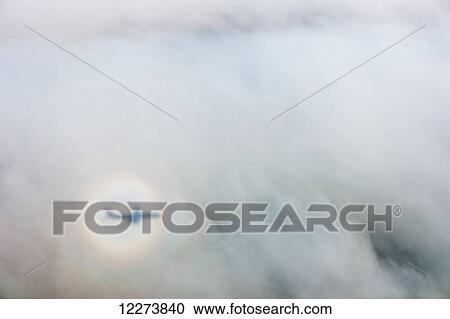 Stock Image - The shadow of an airplane cast by a sundog on clouds; Alaska, United States of America. Fotosearch