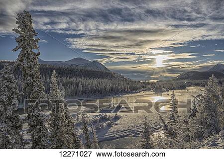 Stock Photo - The sun breaks through the clouds above the Takhini River on a late winter afternoon, near Whitehorse; Yukon, Canada. Fotosearch