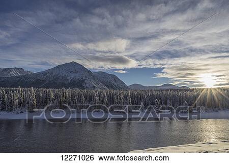 Stock Photograph - The sun breaks through the clouds above the Takhini River on a late winter afternoon, near Whitehorse; Yukon, Canada. Fotosearch