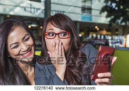 Stock Image - Two businesswomen taking a self-portrait in a coffee shop in a shopping complex; St. Albert, Alberta, Canada. Fotosearch