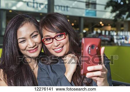 Two businesswomen taking a self-portrait in a coffee shop in a shopping complex; St. Albert, Alberta, Canada View Large Photo Image Stock Image - Two businesswomen taking a self-portrait in a coffee shop in a shopping complex; St. Albert, Alberta, Canada. Fotosearch