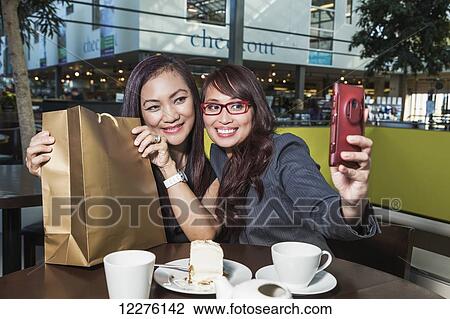 Two businesswomen taking a self-portrait in a coffee shop in a shopping complex with a surprise purchase; St. Albert, Alberta, Canada View Large Photo Image Stock Image - Two businesswomen taking a self-portrait in a coffee shop in a shopping complex with a surprise purchase; St. Albert, Alberta, Canada. Fotosearch