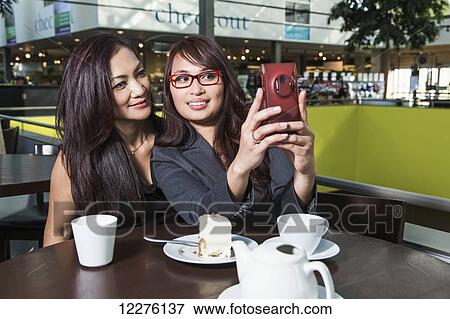 Two businesswomen taking a self-portrait in a coffee shop in a shopping complex; St. Albert, Alberta, Canada View Large Photo Image Stock Photo - Two businesswomen taking a self-portrait in a coffee shop in a shopping complex; St. Albert, Alberta, Canada. Fotosearch