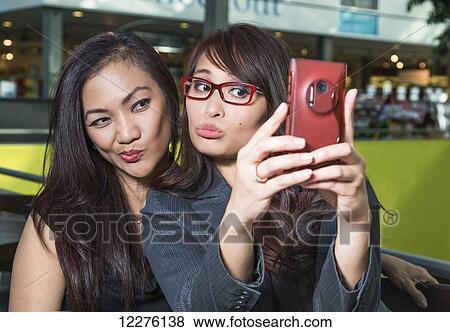 Two businesswomen taking a self-portrait in a coffee shop in a shopping complex; St. Albert, Alberta, Canada View Large Photo Image Stock Photo - Two businesswomen taking a self-portrait in a coffee shop in a shopping complex; St. Albert, Alberta, Canada. Fotosearch