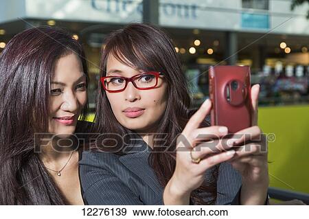 Two businesswomen taking a self-portrait in a coffee shop in a shopping complex; St. Albert, Alberta, Canada View Large Photo Image Stock Photo - Two businesswomen taking a self-portrait in a coffee shop in a shopping complex; St. Albert, Alberta, Canada. Fotosearch