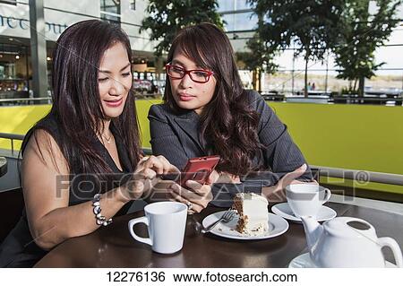 Stock Photograph - Two businesswomen texting while taking a break in a coffee shop in a shopping complex; St. Albert, Alberta, Canada. Fotosearch