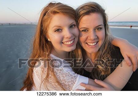 Stock Photograph - Two young women posing on the beach in an embrace at sunset; United States of America. Fotosearch