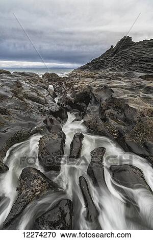 Stock Image - Water rushes over the volcanic bedrock around the area of Tow Hill on the North shore of Haida Gwaii, Naikoon Provincial Park; British Columbia, Canada. Fotosearch