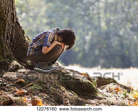 Stock Image - Young boy in a contemplative mood in a forest under an oak tree in a rainforest; Langley, British Columbia, Canada. Fotosearch