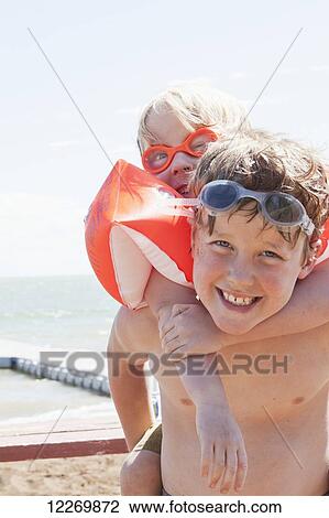 Stock Image - Young brothers play on the sand beach with water and dock in the background; Alberta, Canada. Fotosearch
