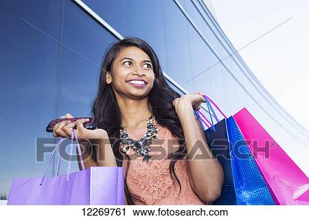 Stock Image - Young businesswoman with shopping bags in an urban setting; Edmonton, Alberta, Canada. Fotosearch