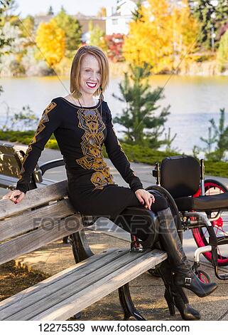 Young disabled woman out of her wheelchair sitting on a bench in a city park in autumn; Edmonton, Alberta, Canada View Large Photo Image Stock Photo - Young disabled woman out of her wheelchair sitting on a bench in a city park in autumn; Edmonton, Alberta, Canada. Fotosearch