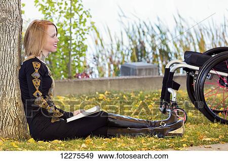 Stock Photo - Young disabled woman sitting beside her wheelchair reading a book in a city park in autumn; Edmonton, Alberta, Canada. Fotosearch