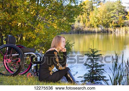 Stock Photograph - Young disabled woman sitting beside her wheelchair in a city park in autumn; Edmonton, Alberta, Canada. Fotosearch