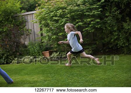 Stock Photo - Young girl running in a backyard; Picton, Ontario, Canada. Fotosearch