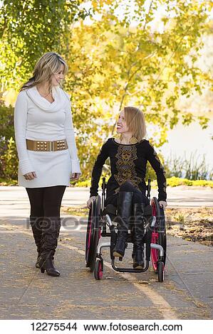 Picture - Young paraplegic woman and her friend spending quality time together in a city park in autumn; Edmonton, Alberta, Canada. Fotosearch